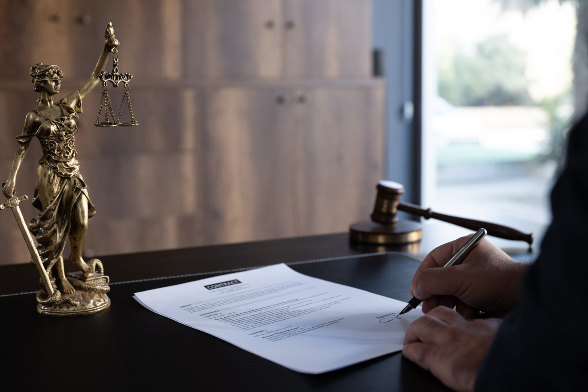 A person signing a legal document on a desk with a gavel nearby.