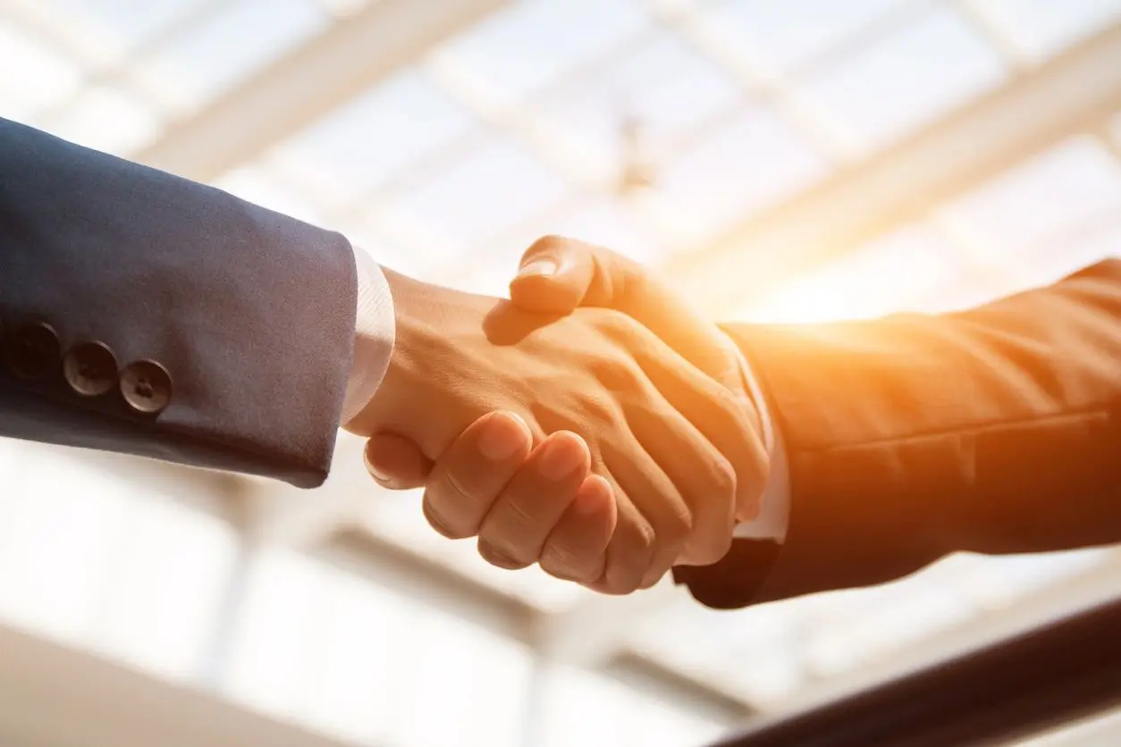 Two people shaking hands in a bright office setting.