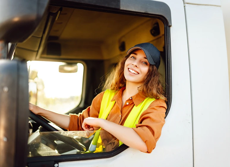 Smiling female truck driver wearing a safety vest and cap.