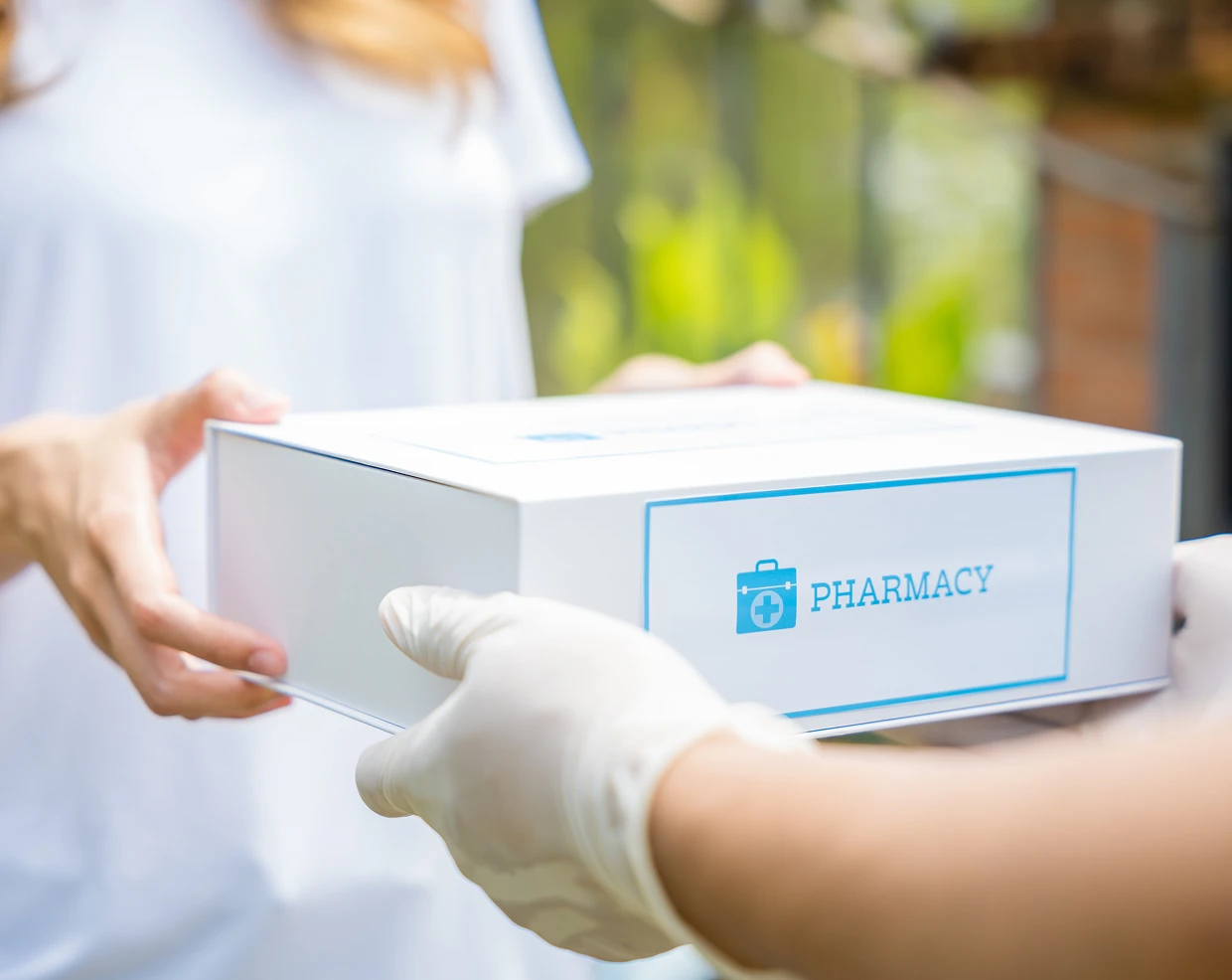 Pharmacy delivery box handed over by a gloved person.